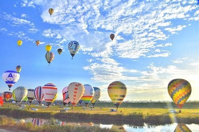 カラフルな気球がたくさん空や平野に漂っている写真
