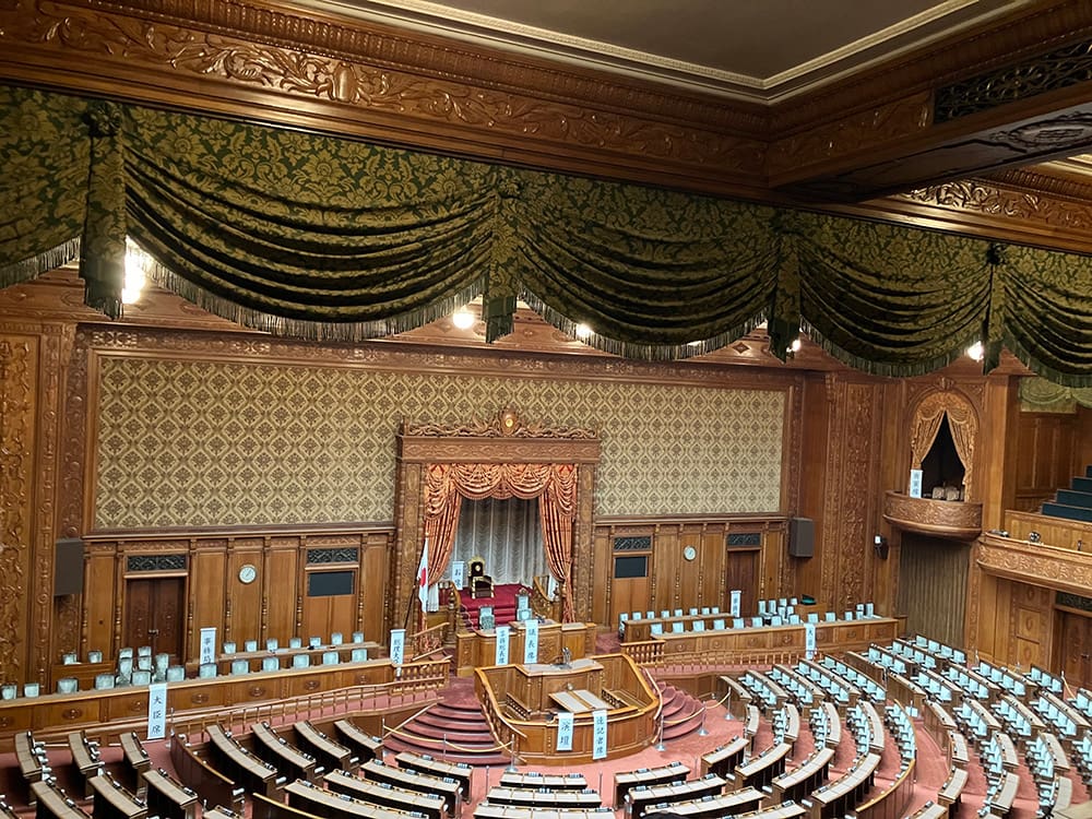 無人の参議院議場内を上から撮った写真。議長席を中心に扇形に席が並んでいる。非常に豪華な室内。