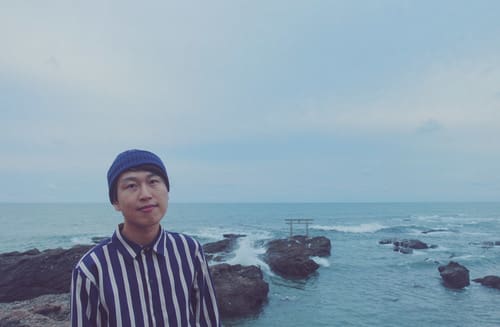 海を背景に香港出身の新しい男性社員のマイクがたっている写真です。