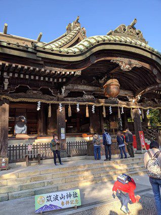 筑波山神社の拝殿前で参拝をしている。頭上の巨大な屋根からは大きな鈴が吊り下げられている。