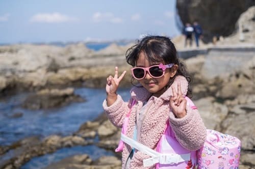 岩場でサングラスをかけたイナーヤちゃんが両手でピースサインをしている