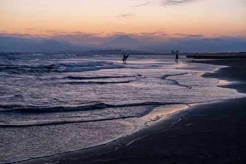 夕焼けをバックにした波打ち際の写真。夕焼けにうっすらと富士山のシルエットが重なっている。