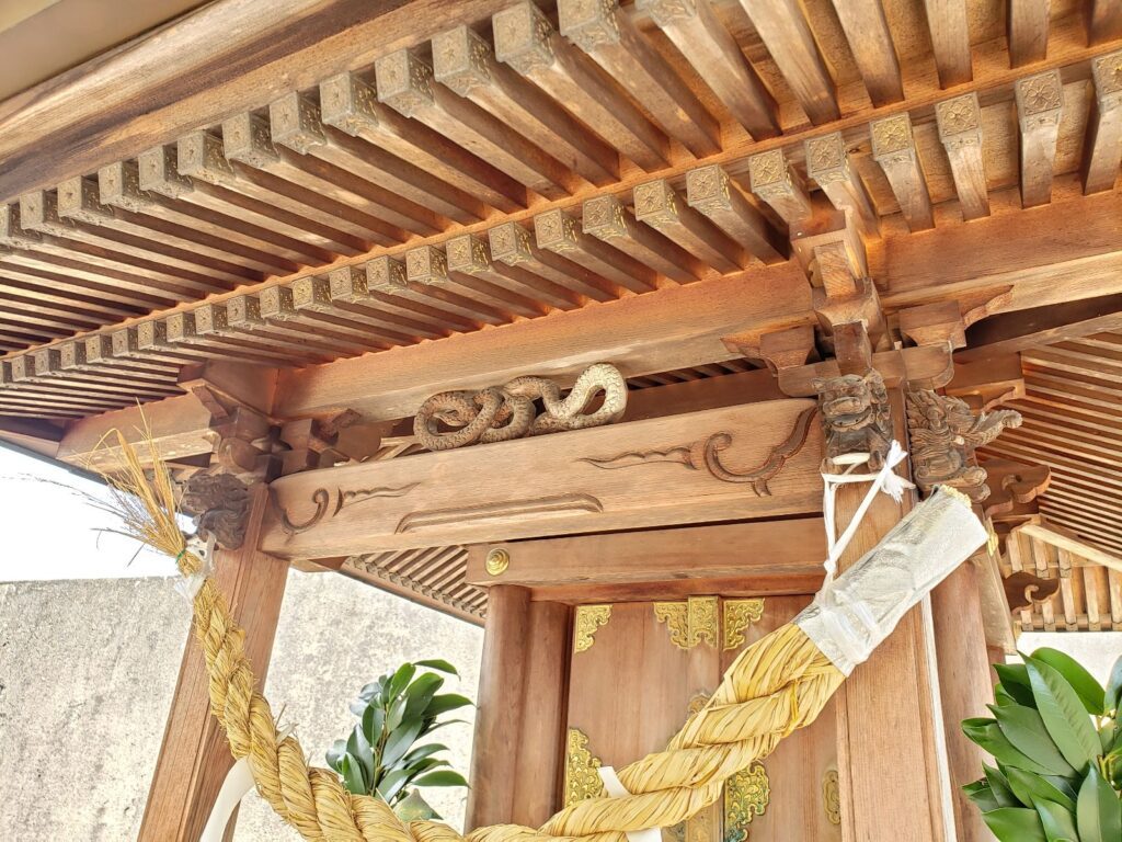 白蛇神社の境内社の虹梁とその上にある木材で作られている彫刻の蛇。