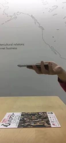 机の上にQRコードが付いたチラシがあり、そのQRコードをスマホで読み取ろうとしている様子。