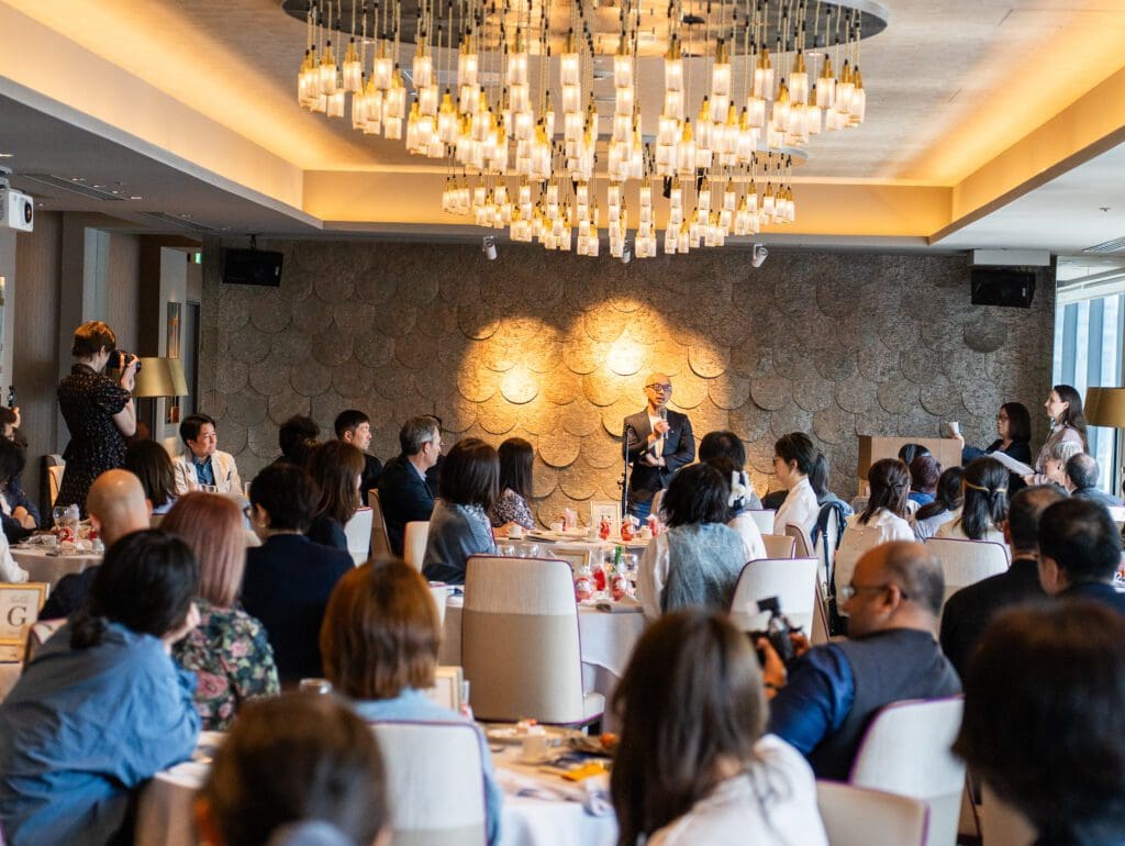 閉会の挨拶をしている高岡を遠景にして撮影した写真で、手前には参加者のテーブルがうつっている