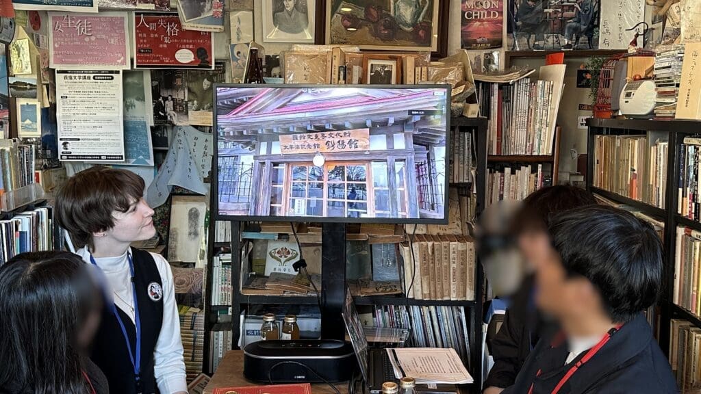 「古本カフェ　フォスフォレッセンス」店内で参加者と一緒に斜陽館と生中継を視聴している弊社スタッフのジェイリーン。