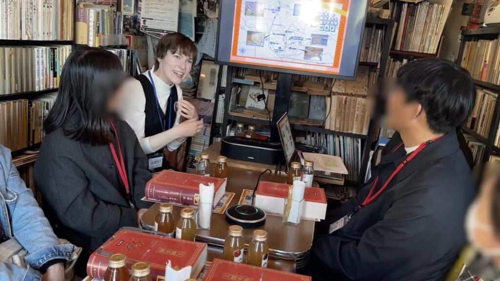 「古本カフェ　フォスフォレッセンス」店内で、弊社スタッフのジェイリーンが「太宰治の聖地巡礼＆金木町散策MAP」を参加者に紹介する。