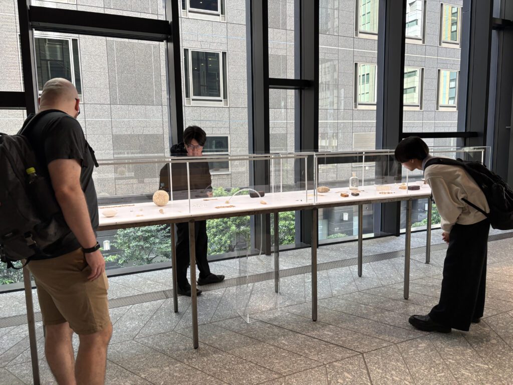 3人の男性がガラスケースの中の作品を鑑賞しています。
