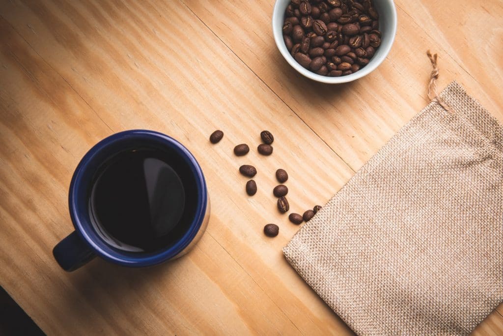 コーヒー豆の入ったカップ、コーヒーを淹れた紺色のカップが木製のテーブル上にあり、テーブルには数個のコーヒー豆があります。