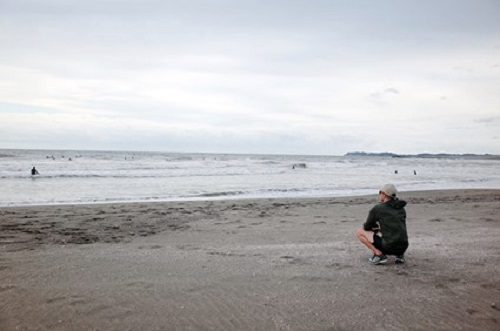 浜辺で海を眺めながら座っている佐藤さん。