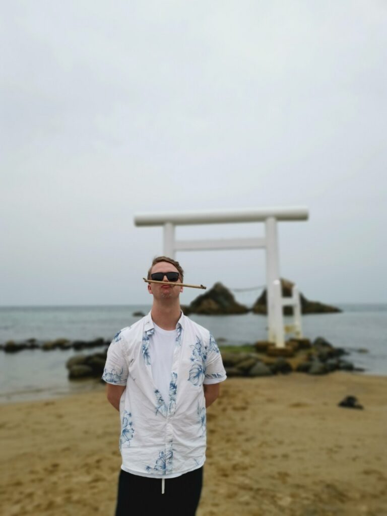 背景に白い鳥居、前にライアンがたっている写真です。