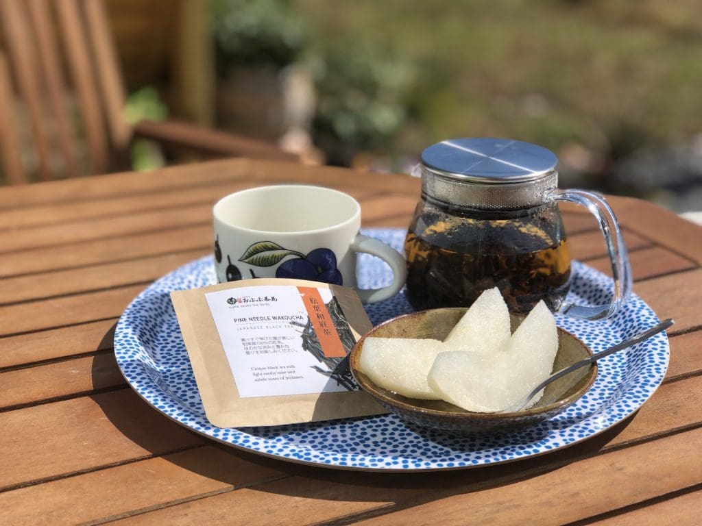 屋外のテーブルに、透明急須に和紅茶、梨と一緒にティーカップが並んでいます。