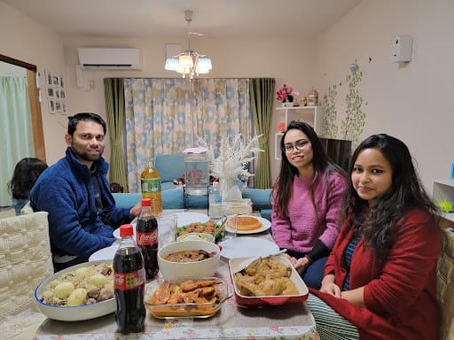 お料理がたくさん載った自宅のダイニングテーブルに男性1人と女性2人が座っている