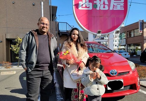 イフテカールさん、花束を持った奥さん、娘さんの後ろに赤い車が写っている